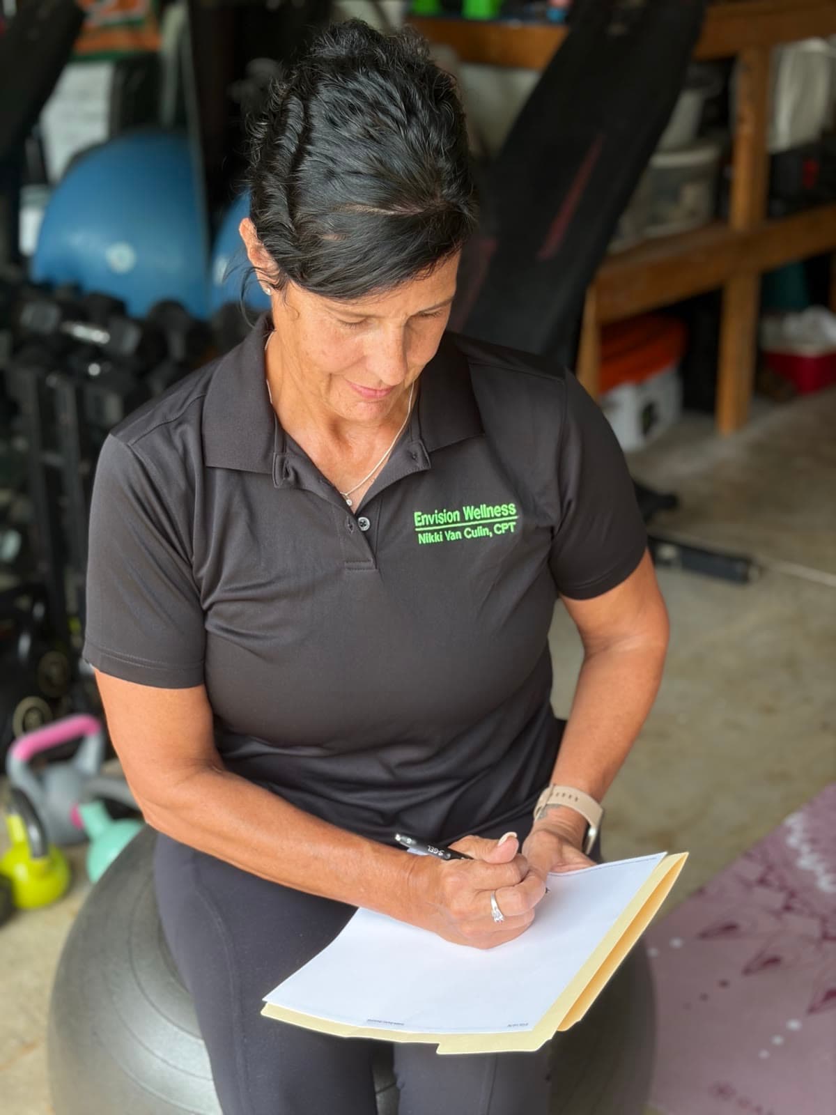 Nikki Van Culin sitting on a stability ball in her studio, writing out a client’s program