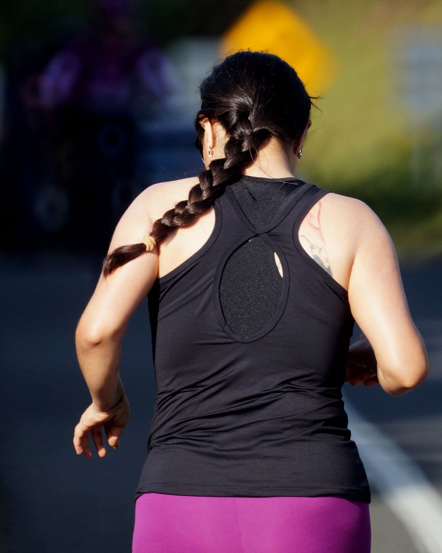 A woman with a long braid running along a country road, seen from behind